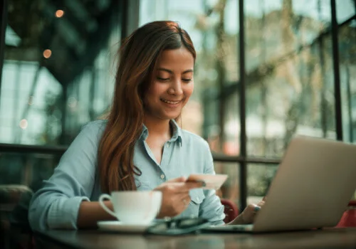 A gild holding her new credit card and using her laptop on a coffee shop