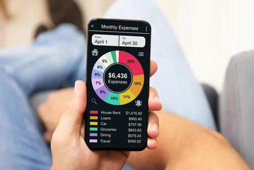 person sitting down and looking at their phone which is displaying a budgeting app