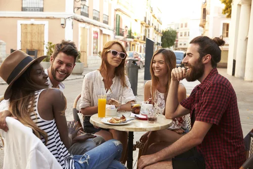 Group of Millennials sitting at a table outside eating and laughing