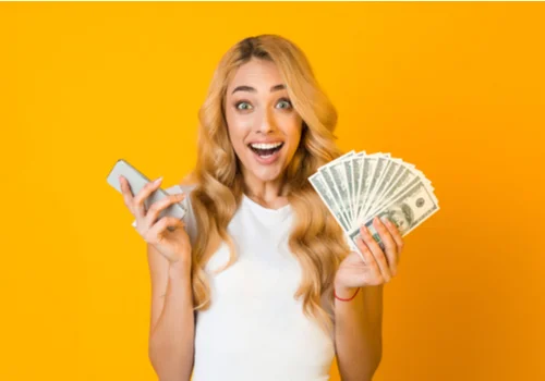 a happy woman holding her pay check seven days early and her phone.