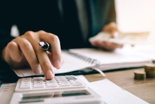 person holding a pen and typing on a calculator