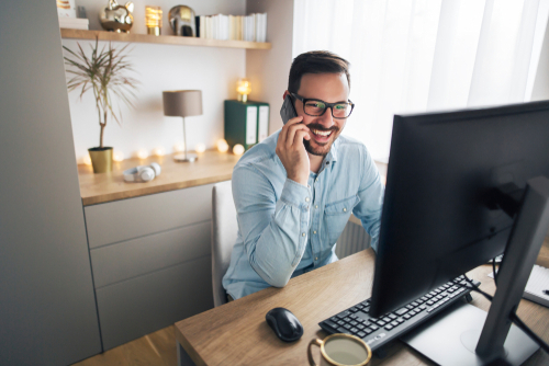 Happy gentleman lookin at a desktop and talking on the phone. 