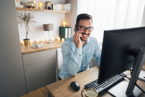 Happy gentleman lookin at a desktop and talking on the phone.