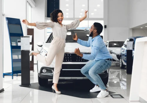 a couple just bought their first car and she woman is jumping up