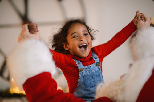 child with an excited facial expression holding hands with Santa