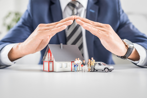 man holding hands over miniature house and car