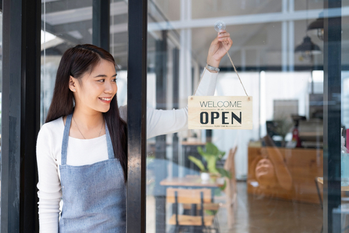 woman putting up now open sign at business