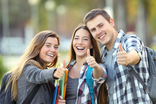 students giving thumbs up holding books and wearing backpacks