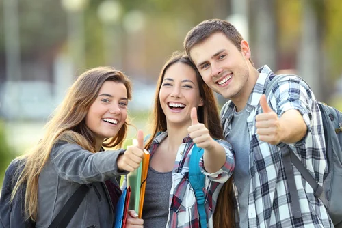 students giving thumbs up holding books and wearing backpacks