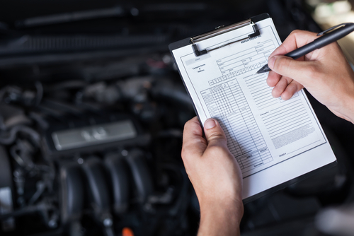 person completing car checklist with hood open