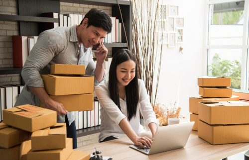 man and woman looking at computer holding boxes