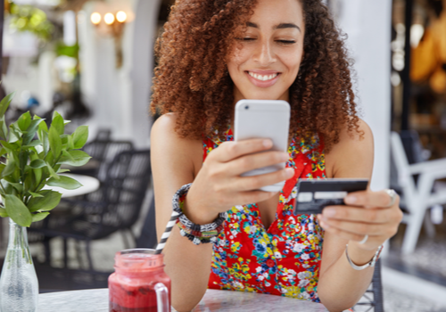 A girl holding her credit card and looking the benefits she gets on ger phone. 