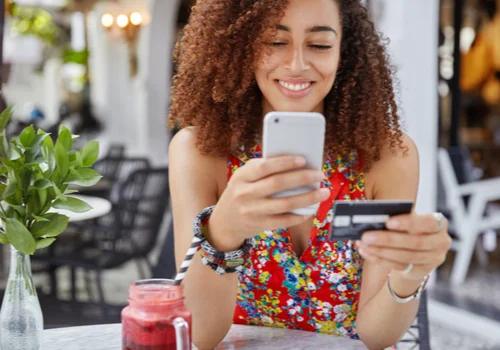 A girl holding her credit card and looking the benefits she gets on ger phone.