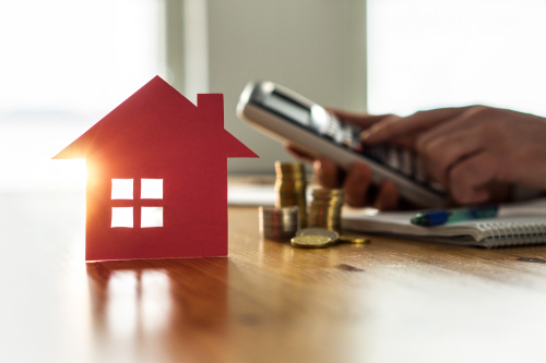 person using a calculator on desk and cutout of a house 