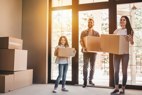 family holding boxes and entering new home