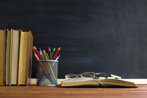 books pencils and glasses on a desk in front of a chalk board