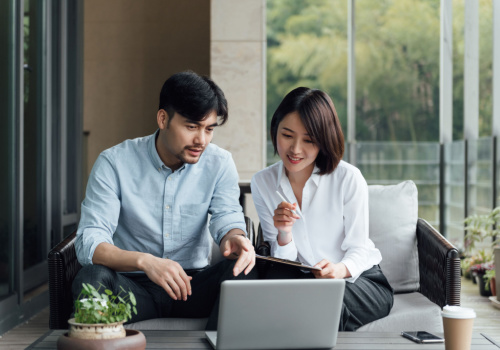 A couple looking at stuff on their laptop and the husbands points something out to his wife