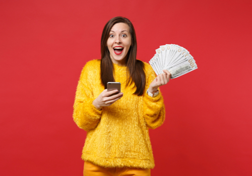 a happy woman holing up money on her right hand and her phone on her left hand. 