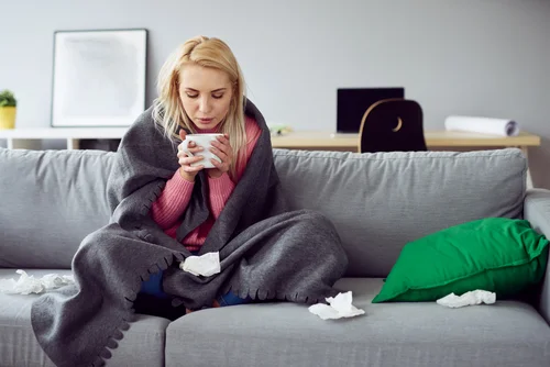 woman on a couch holding cup and covered in a blanket