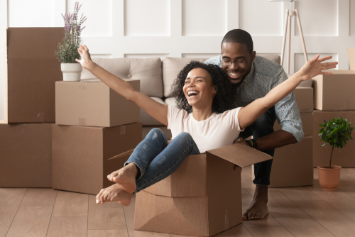 woman is inside of cardboard box with arms up while man pushes her across the floor