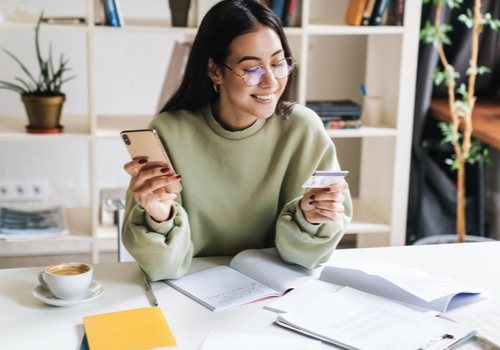 A young lady holding her new credit card and activating it on her phone.