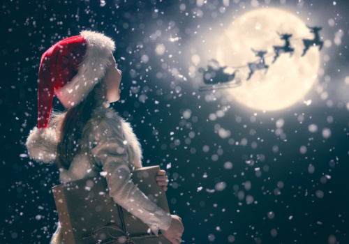 a little kid wearing a Santa hat looking up at Santa Claus in the night 