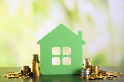 Green cutout of a home with various coins stacked around it 