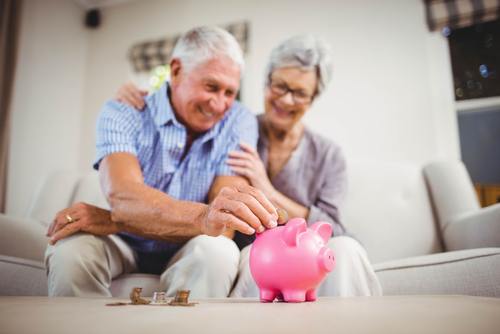 older couple sitting on the couch and putting coins into a pink piggy bank