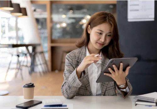 a happy woman in a coffee shop holding her iPad and opening a new checking account.