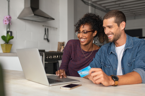man and woman smiling holding credit card looking at computer screen