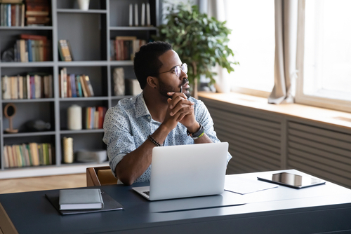 Man sitting in office looking out window with laptop in front of him