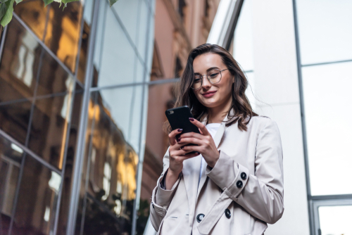 woman outside in front of building looking down at her phone