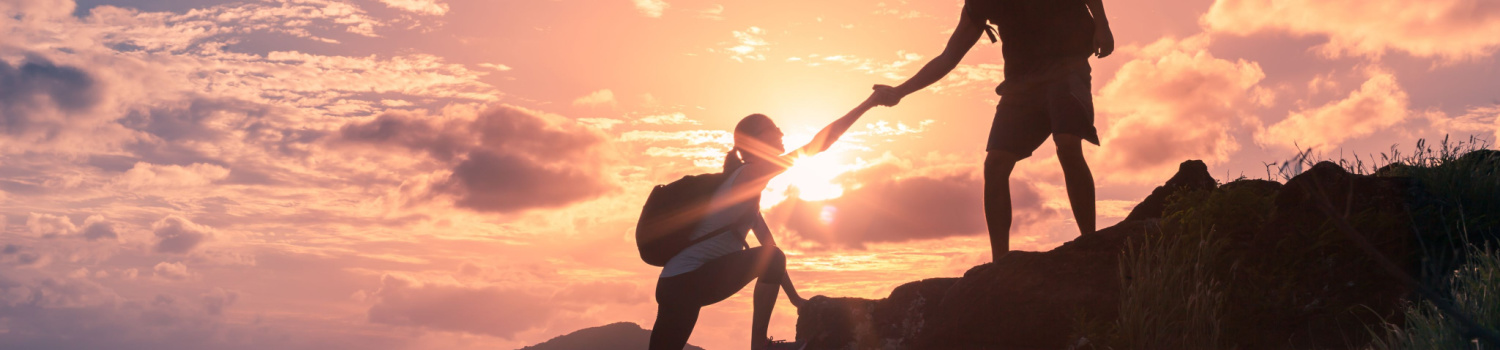 a gentlemen helping a lady climb rocks as the sun sets 