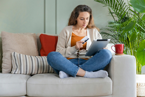 woman sitting on couch looking at computer screen and holding a credit or debit card