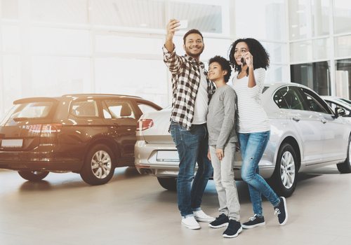 a family taking a selfie in front of their new car 