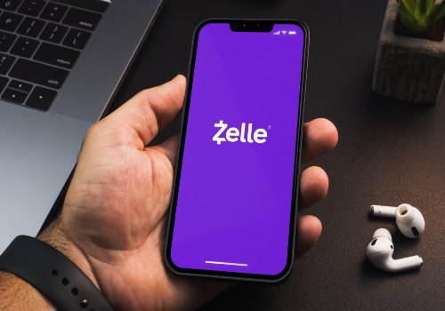 A person holding a phone with the "Zelle" app open 